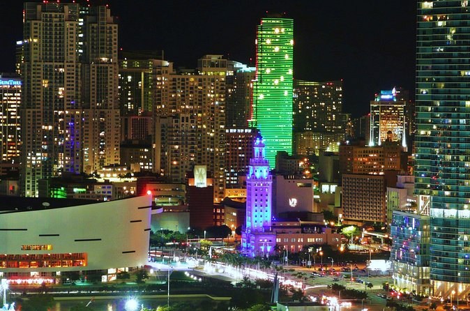 Downtown at night from above, a green-lit tower and a floodlit historic tower below