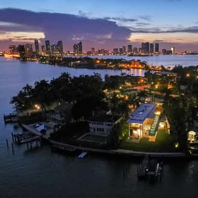 The bay islands from above at dusk, lit homes in the trees and the skyline beyond