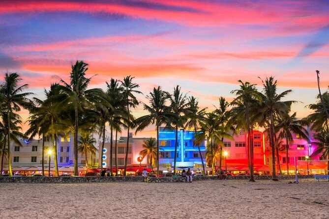 The Art Deco hotels of Ocean Drive lit in neon under a sunset sky, palms along the sand