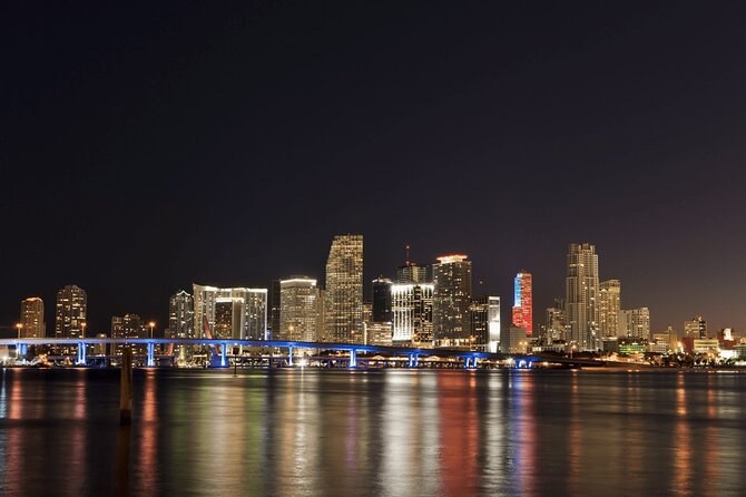 The downtown skyline at night across the water, a lit causeway reflected in the bay