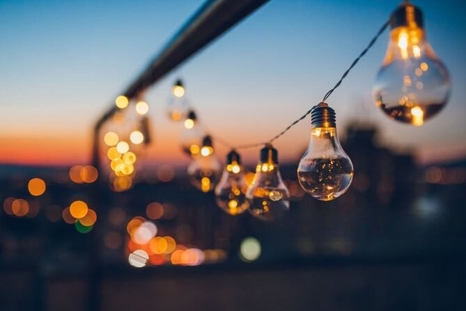 String lights along a boat rail at dusk, the city blurred behind